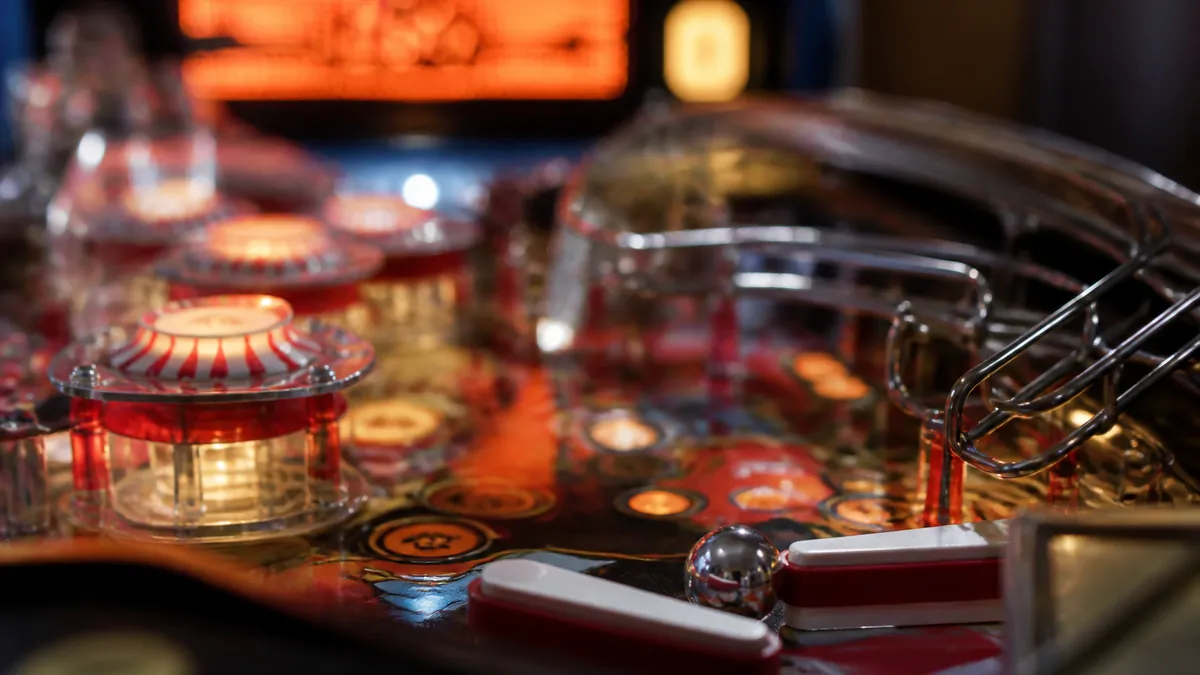 Gros plan sur le plateau de jeu d'un flipper avec ses rampes, ses bumpers et son écran à matrice de points allumé