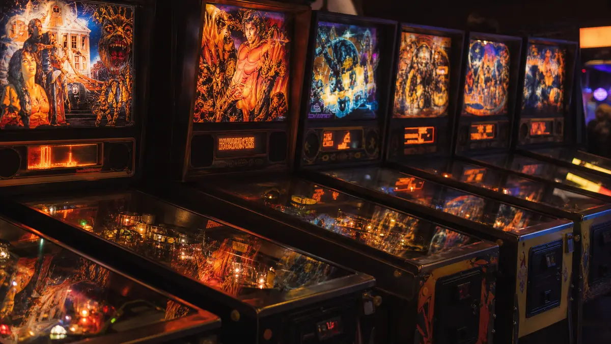 Rangée de flippers cultes des années 90 alignés dans une salle d'arcade sombre aux néons colorés
