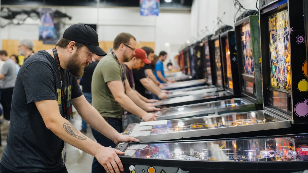 Rangée de flippers alignés dans une salle de tournoi avec des joueurs en compétition